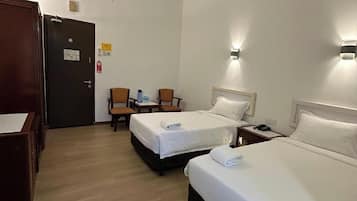 Habitación de hotel con dos camas, un escritorio, dos sillas, una puerta y una lámpara fijada a la pared.