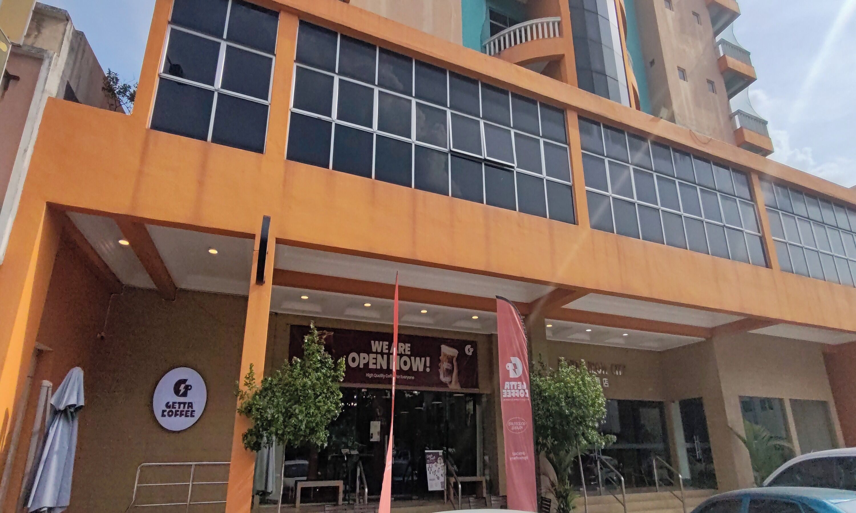 A building with a large glass facade, a sign for a coffee shop, and a red banner indicating the establishment is open.