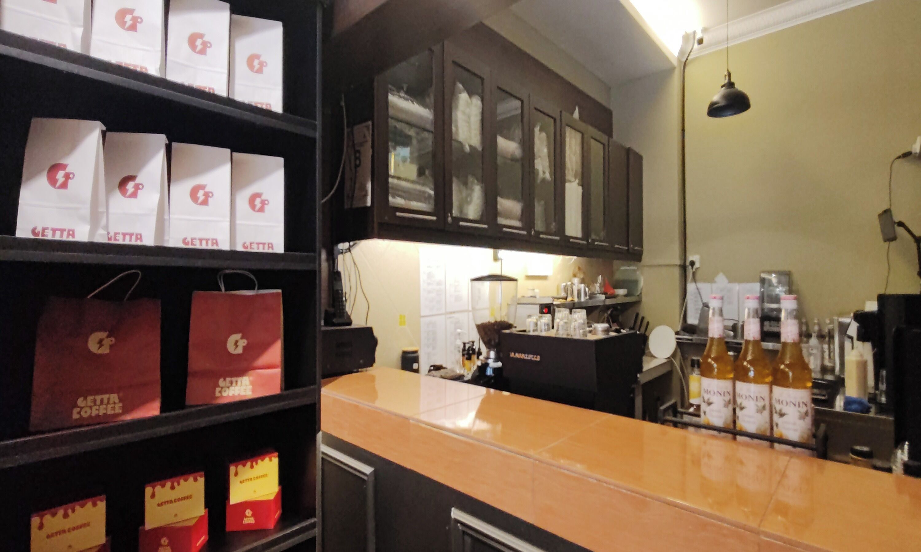 A kitchen area with shelves stocked with branded coffee bags, a counter with coffee-making equipment, and cabinets above.