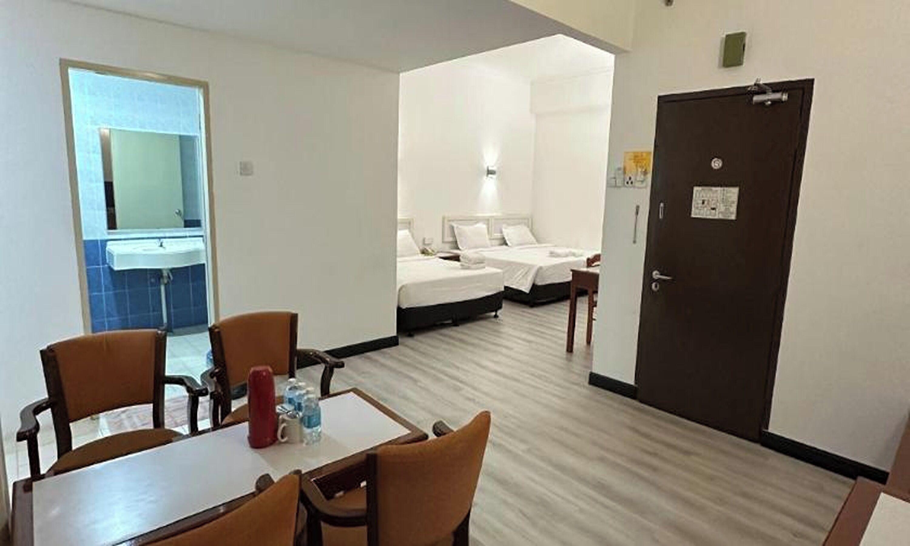 A hotel room with a dining area, two beds, a bathroom, and a door.
