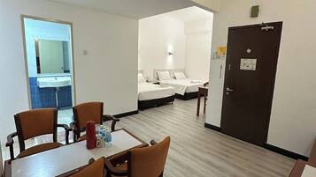 A hotel room with a dining area, two beds, a bathroom, and a door.