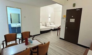 Quarto de hotel com área de jantar, duas camas, banheiro e porta.