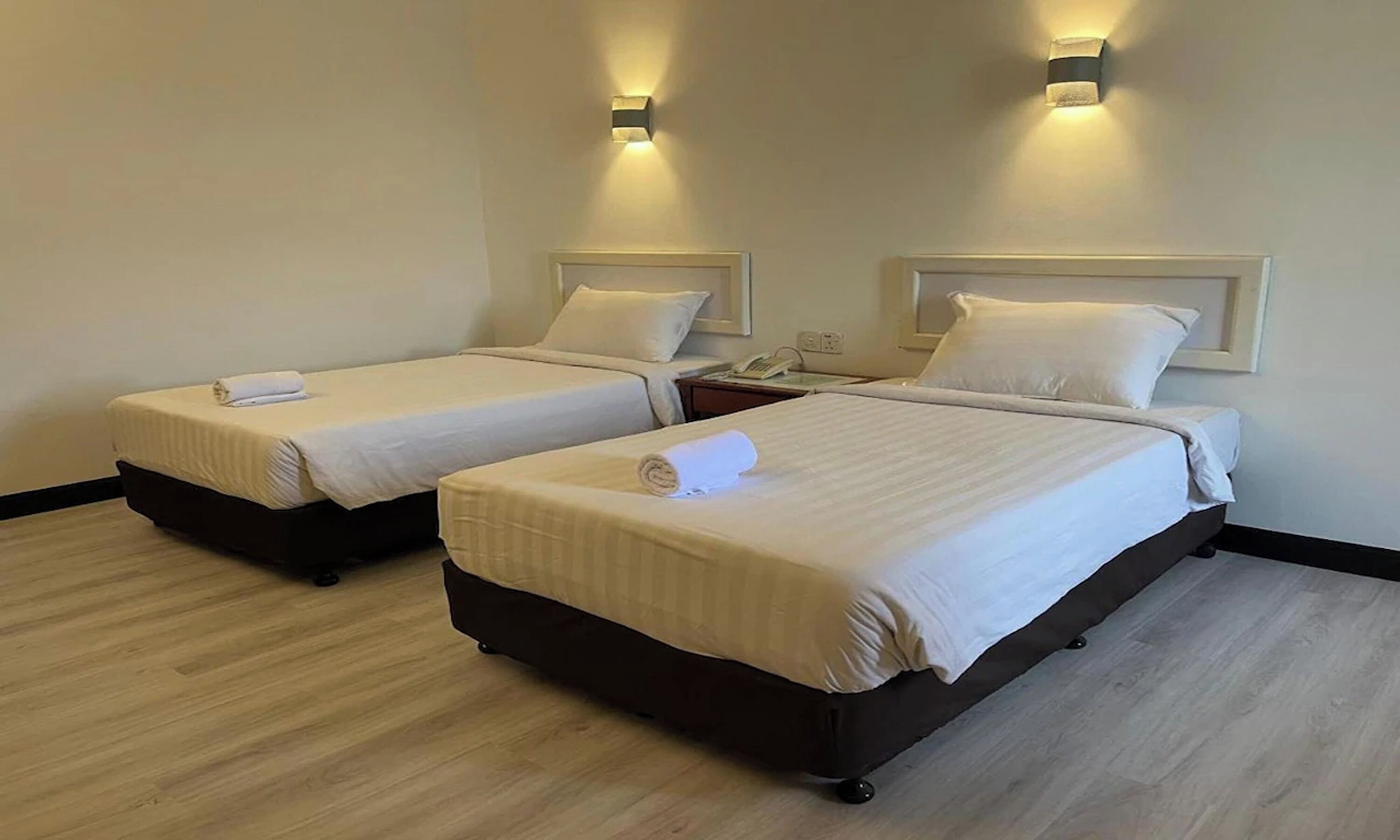 Une chambre d’hôtel avec deux lits, chacun équipé d’un oreiller et d’une serviette enroulée. Des appliques murales sont fixées au-dessus des lits.