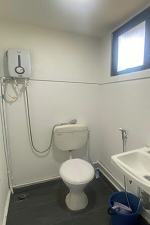 Un baño pequeño con inodoro, lavamanos y ventana sobre el lavabo.