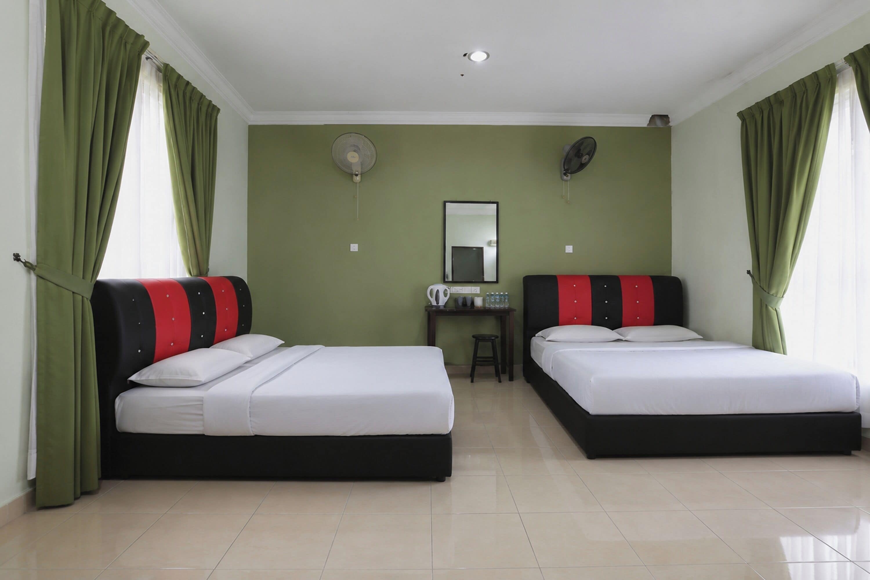 A hotel room with two beds, a desk, a chair, a mirror, and a ceiling fan.