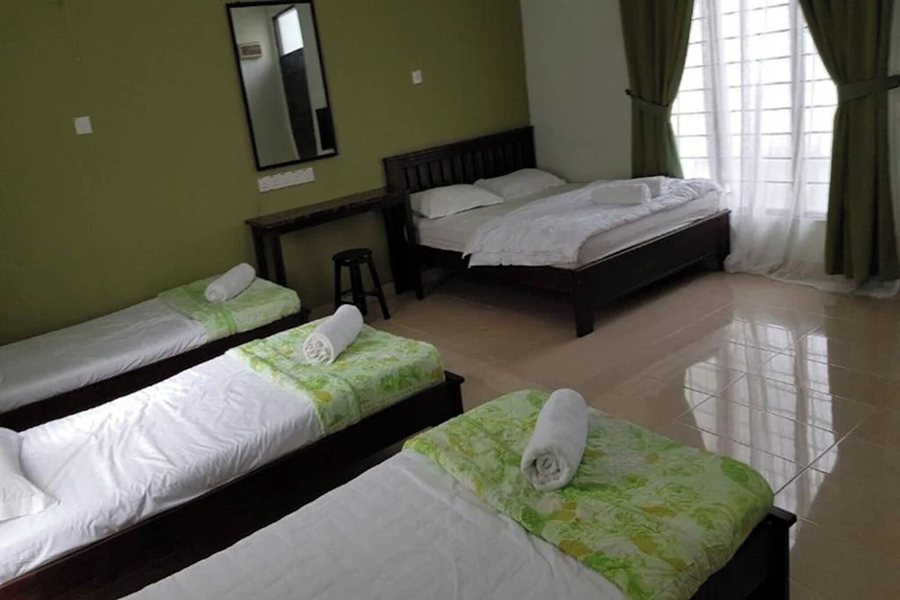 Habitación de hotel con tres camas individuales, un escritorio y un espejo en la pared.