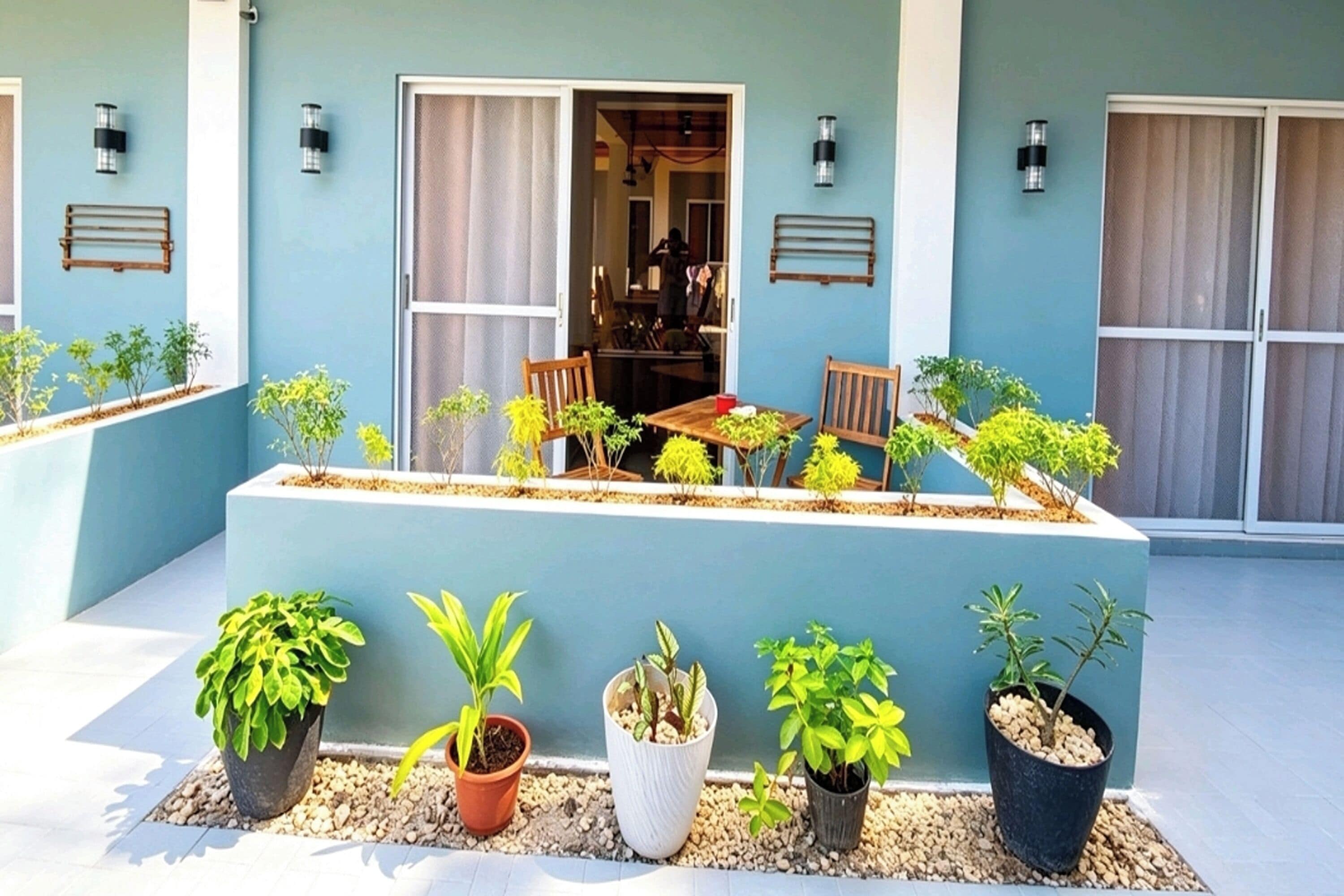 Un bâtiment à la façade bleue, doté d’un espace extérieur abrité avec des tables et des chaises, ainsi que de plantes en pot.