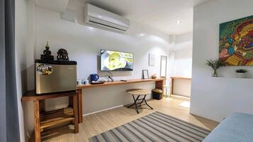 A compact living space with a kitchenette, a flat-screen TV mounted on the wall, a small wooden table, a single chair, and a colorful artwork on the wall.