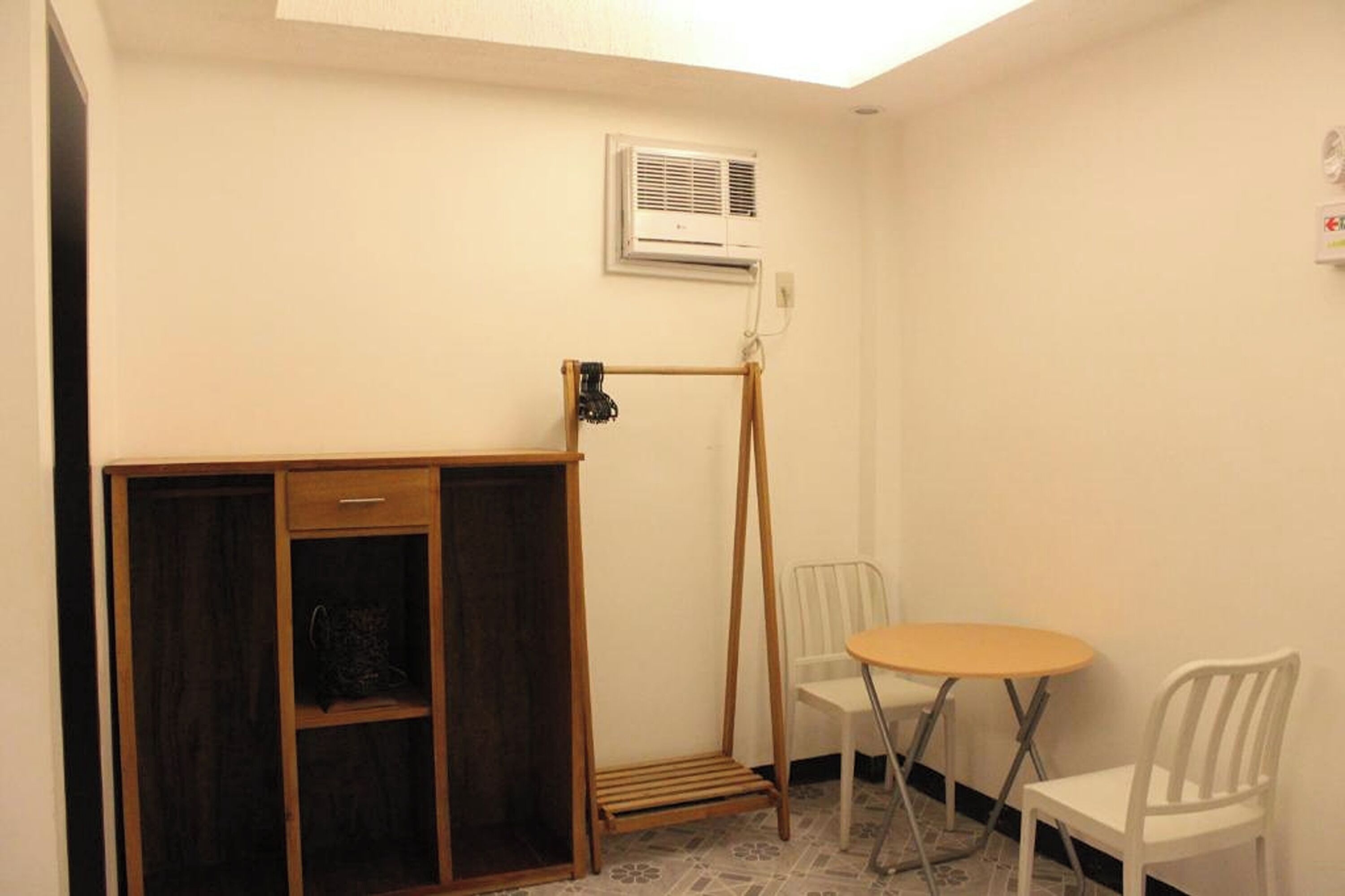 Une petite pièce avec un meuble en bois, une table et deux chaises, ainsi qu’un radiateur portatif.