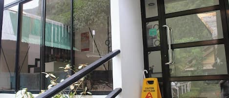 Entrada de un hotel con puerta de vidrio, señal de precaución amarilla y baranda de metal.