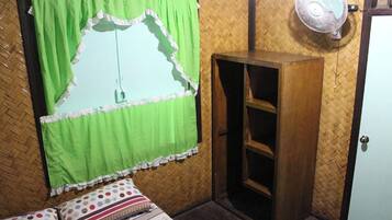 A room with a bed, a wooden wardrobe, a fan, and a window with a green curtain.