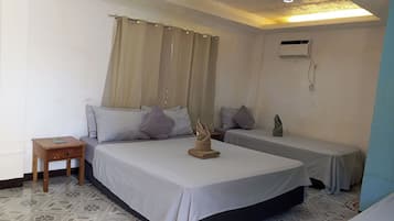 A hotel room with two single beds, a small wooden nightstand, a wall-mounted air conditioning unit, and a patterned floor.