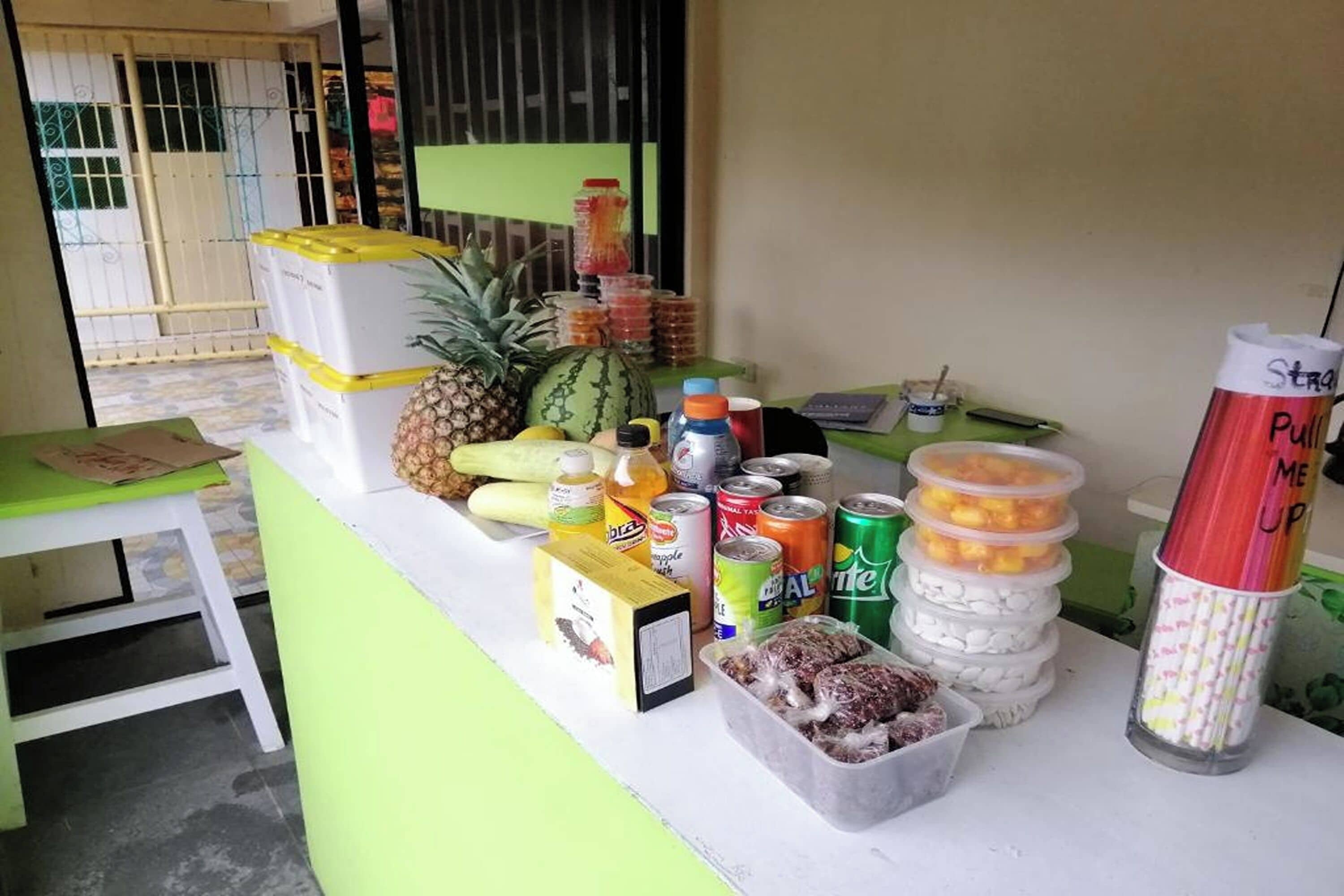 A counter with various food items and drinks, including a pineapple, watermelon, and cans of soda.