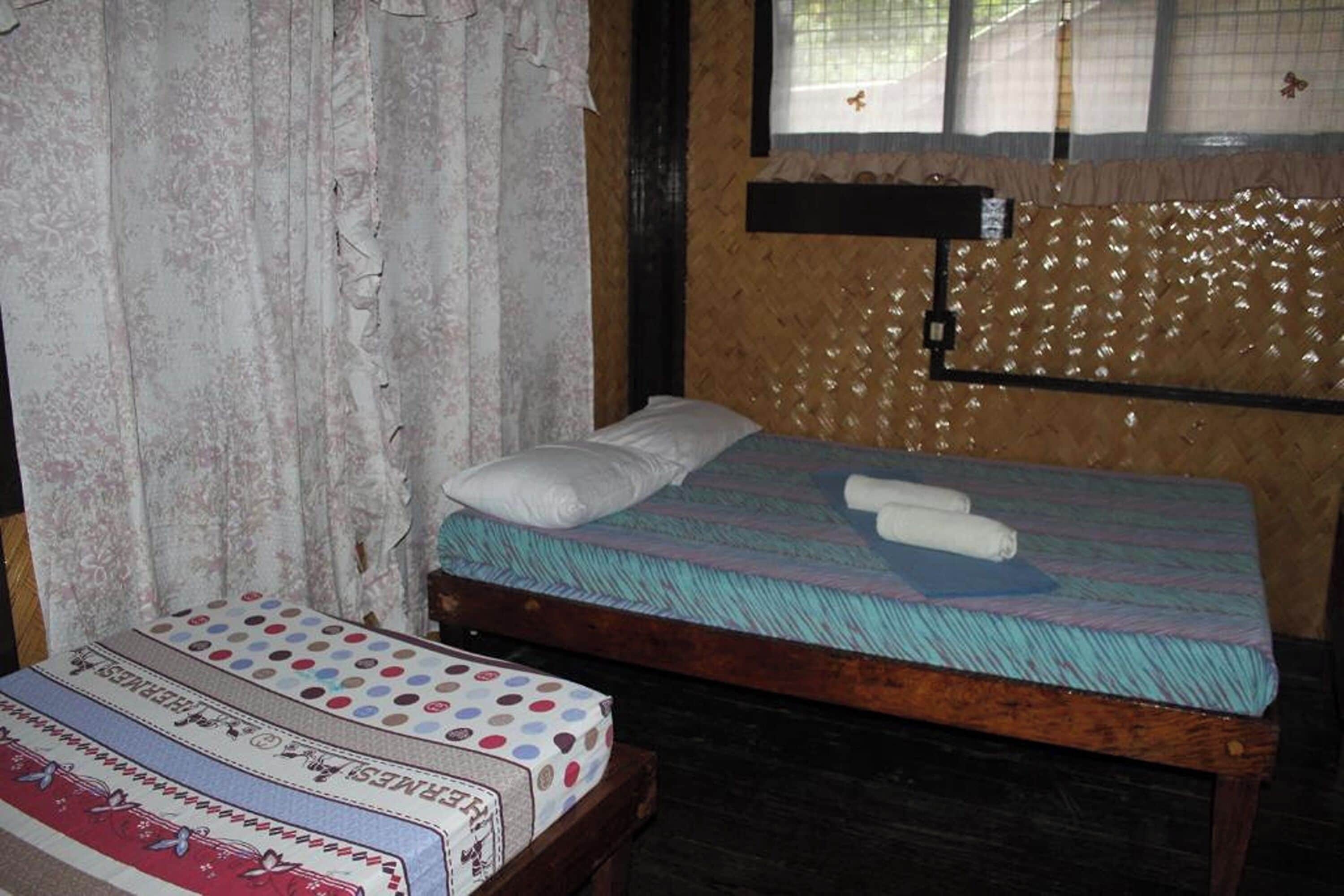 Un lit simple avec un matelas et des oreillers à rayures, une tête de lit en bois et une fenêtre avec des rideaux.
