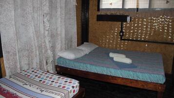 A single bed with a striped mattress and pillows, a wooden headboard, and a window with curtains.