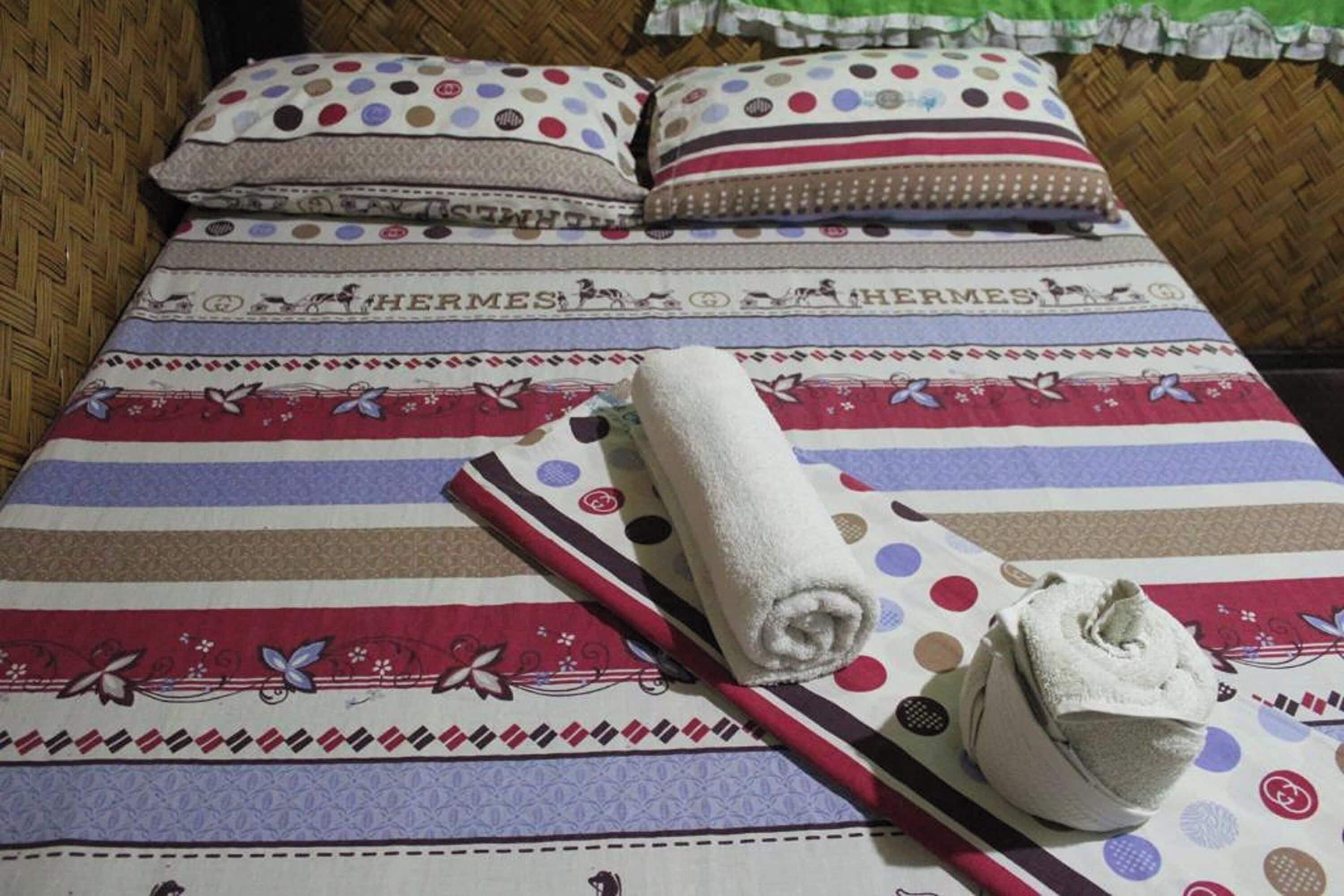 Un lit avec une literie à rayures, deux oreillers, une serviette enroulée et une paire de chaussons.