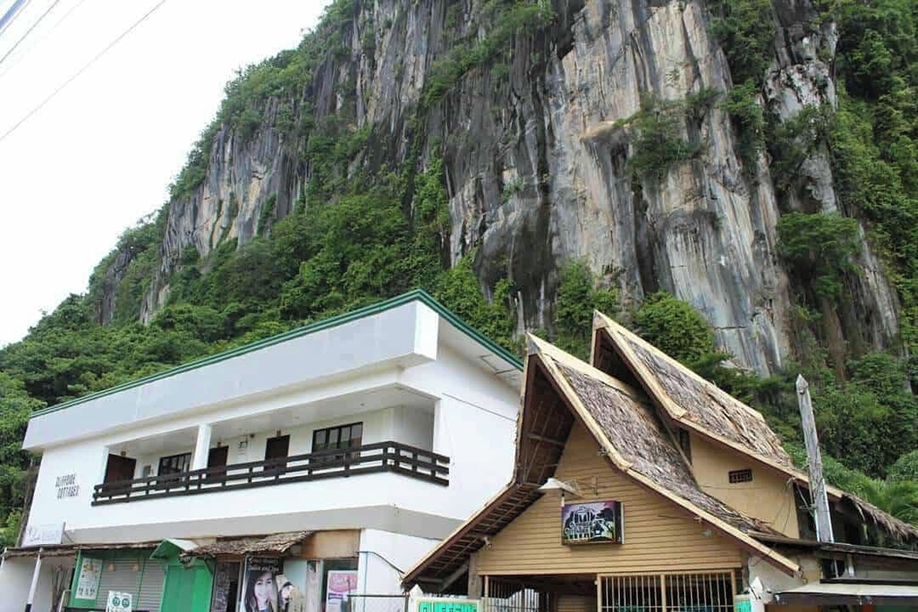 Un edificio con fachada blanca y un balcón, ubicado frente a un acantilado rocoso empinado.