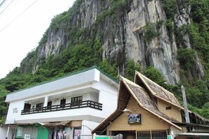 A building with a white facade and a balcony, located in front of a steep, rocky cliff. - Cliffside Cottages (El Nido)