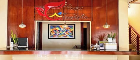 A reception desk with a wooden backdrop, a colorful abstract painting, and a sign that reads 'Casa Teofista.'