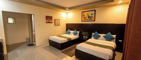A hotel room with two beds, a small table, a wall-mounted TV, and a door leading to a hallway.