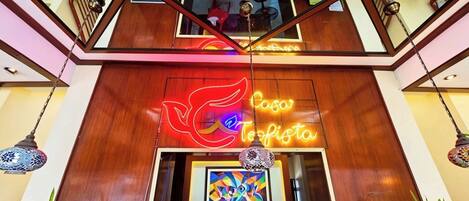 A hotel entrance with a neon sign, a colorful artwork, and a wooden interior.