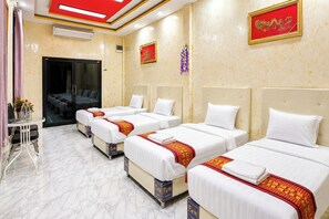 A hotel room with four single beds, a small table with chairs, a bathroom with a glass door, and a red-framed picture on the wall.