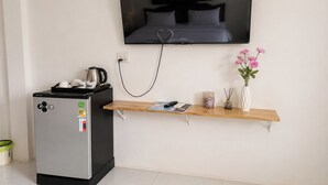Een compacte kitchenette met een koffiezetapparaat, een kleine koelkast en een aan de muur bevestigde televisie.