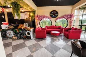 A cafe interior with a coffee machine, seating area, and decorative plants. - White House Hotel Kamphaeng Phet (Kamphaeng Phet)