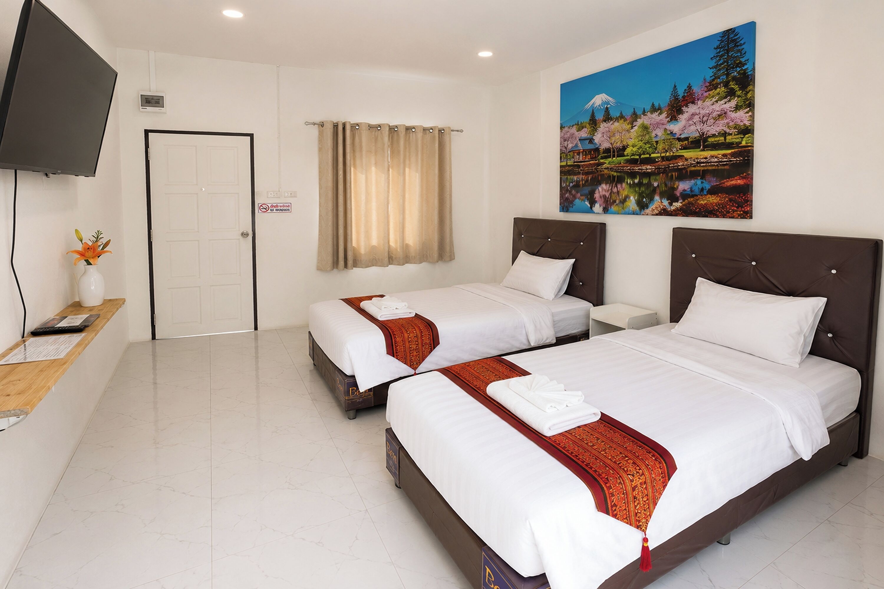A hotel room with two beds, a television, a desk with a vase of flowers, and a painting of a landscape.