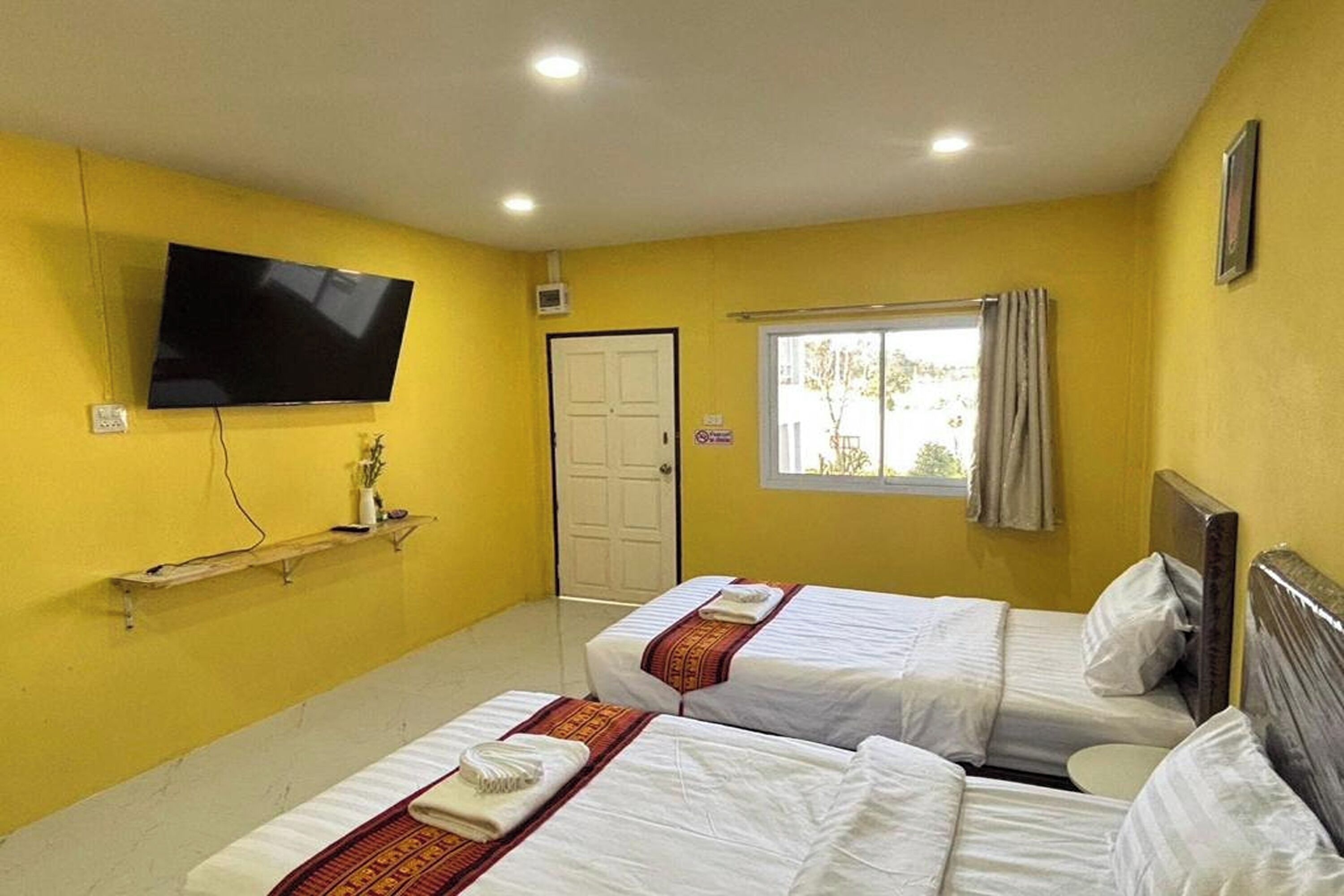 A hotel room with two beds, a television mounted on the wall, a window with curtains, and a door.