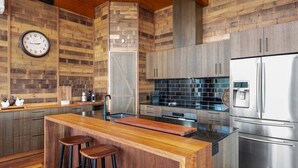 A modern kitchen with wooden cabinetry, a central island with stools, a stainless steel refrigerator, and a clock on the wall. - Ridge Way Views - Breathtaking Lake Eildon Views (Mountain Bay)