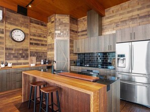 A modern kitchen with wooden cabinetry, a central island with stools, a stainless steel refrigerator, and a clock on the wall. - Ridge Way Views - Breathtaking Lake Eildon Views (Mountain Bay)