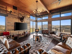 A spacious living room with a large flat-screen TV, leather sofas, a chandelier, and a fireplace. - Ridge Way Views - Breathtaking Lake Eildon Views (Mountain Bay)