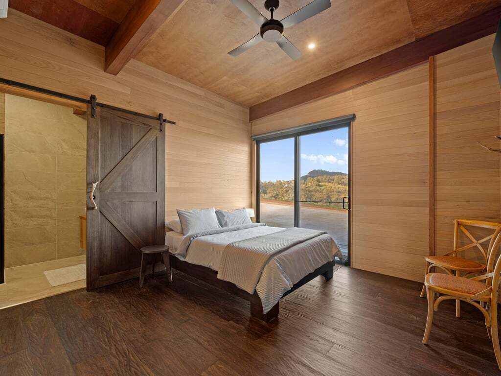 A bedroom with a bed, a chair, a sliding door, and a large window.