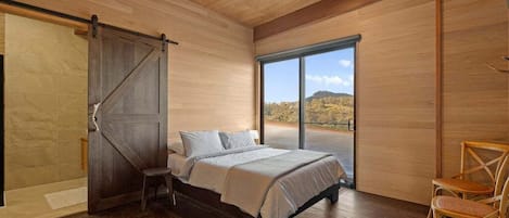 Ein Schlafzimmer mit einem Bett, einem Sessel, einer Schiebetür und einem großen Fenster.