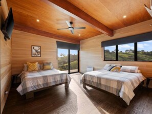 Ein Schlafzimmer mit zwei Betten, einem Deckenventilator und großen Fenstern mit Blick ins Freie.