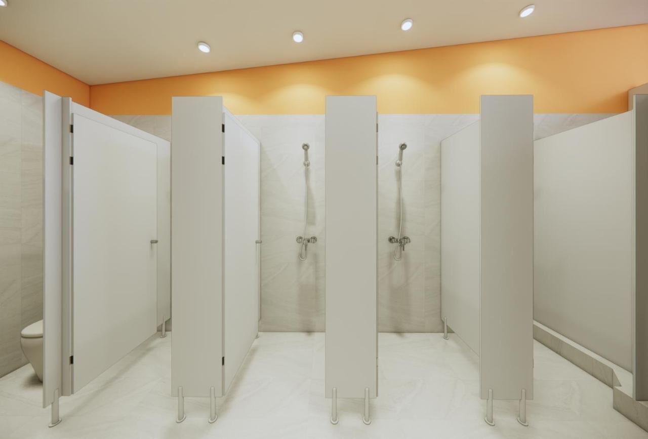 A row of white, wall-mounted shower stalls with a tiled floor and a ceiling with recessed lighting.