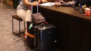 A reception desk with a computer monitor, a man and a woman seated, and a luggage trolley. - Rebel Rooster Hostel (Hanoi)