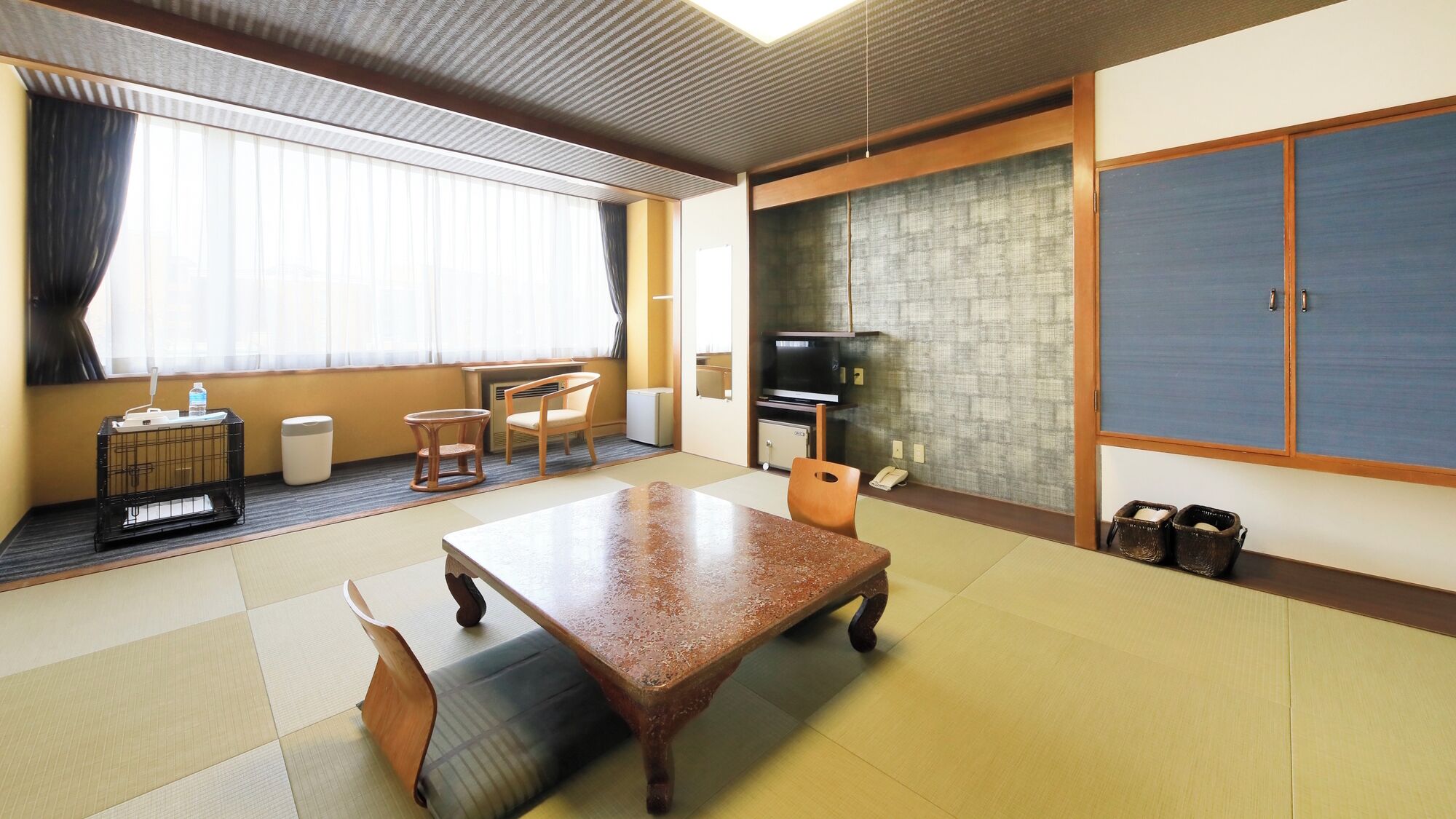 Habitación de hotel con suelo de tatami, una mesa de madera, sillas, un televisor y un armario.