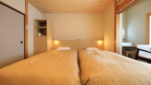 Hotellihuone, jossa on kaksi sänkyä, puinen sängynpääty, pieni työpöytä ja peili.