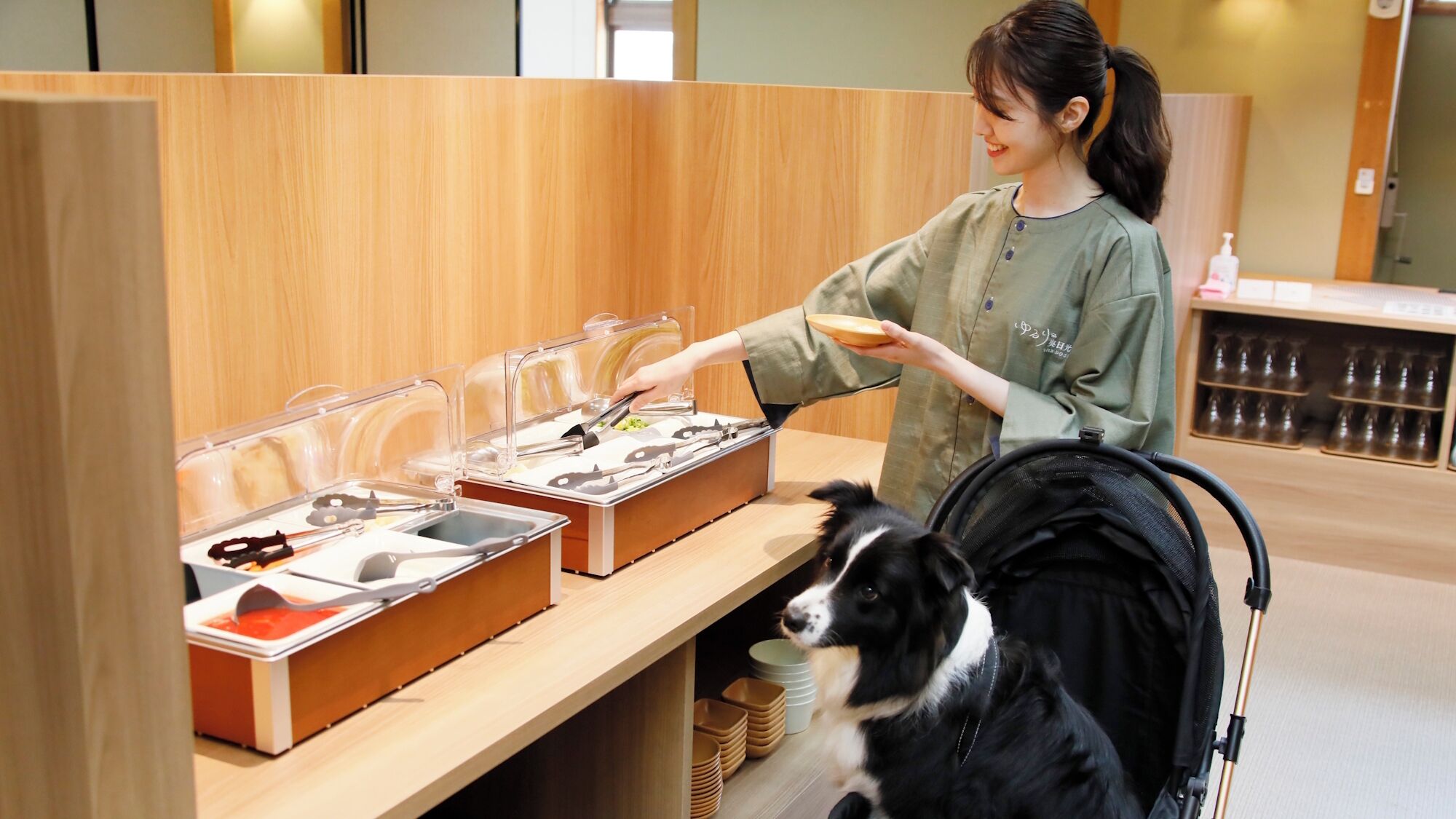 Una persona sirve comida de un bufé con un perro a su lado.