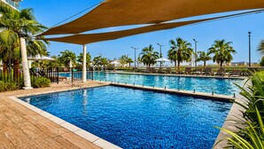 Ein rechteckiger Pool mit gefliestem Sonnendeck, umgeben von Palmen und Liegestühlen.