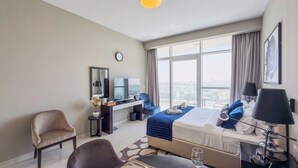 Ein Hotelzimmer mit einem Bett, einem Schreibtisch mit Computer, einem Stuhl, einem Esstisch und einem großen Fenster mit Blick auf die Stadt.