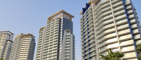 Een meerlaags woongebouw met balkons, een heldere lucht en palmbomen langs de straat.