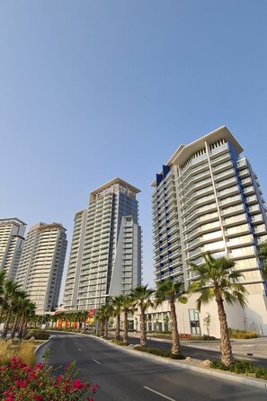 Een meerlaags woongebouw met balkons, een heldere lucht en palmbomen langs de straat.