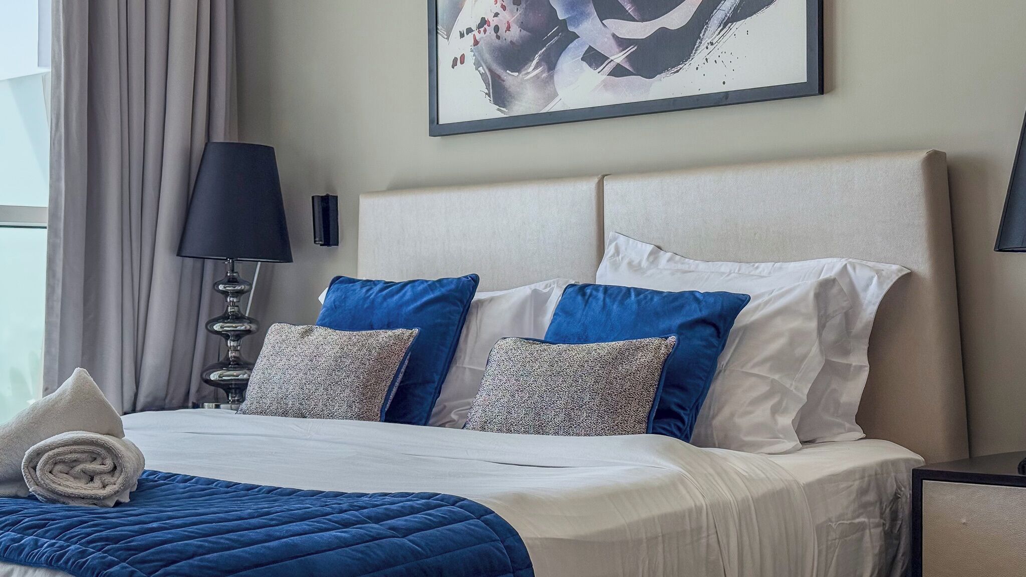 Een hotelkamer met een bed, kussens, een lamp en een schilderij aan de muur.