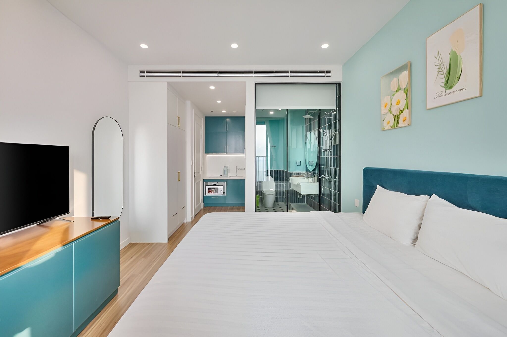 Una habitación de hotel moderna con una cama grande, televisión, baño con cabina de ducha de vidrio y obras de arte en las paredes.
