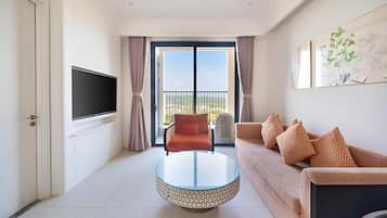 A modern living room with a flat-screen TV, a round glass coffee table, a sofa with patterned cushions, and a balcony with a view.