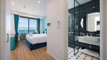 Une chambre d’hôtel moderne dotée d’un balcon, d’un lit, d’un bureau et d’une salle de bain avec un grand miroir et des murs recouverts de carreaux noirs.