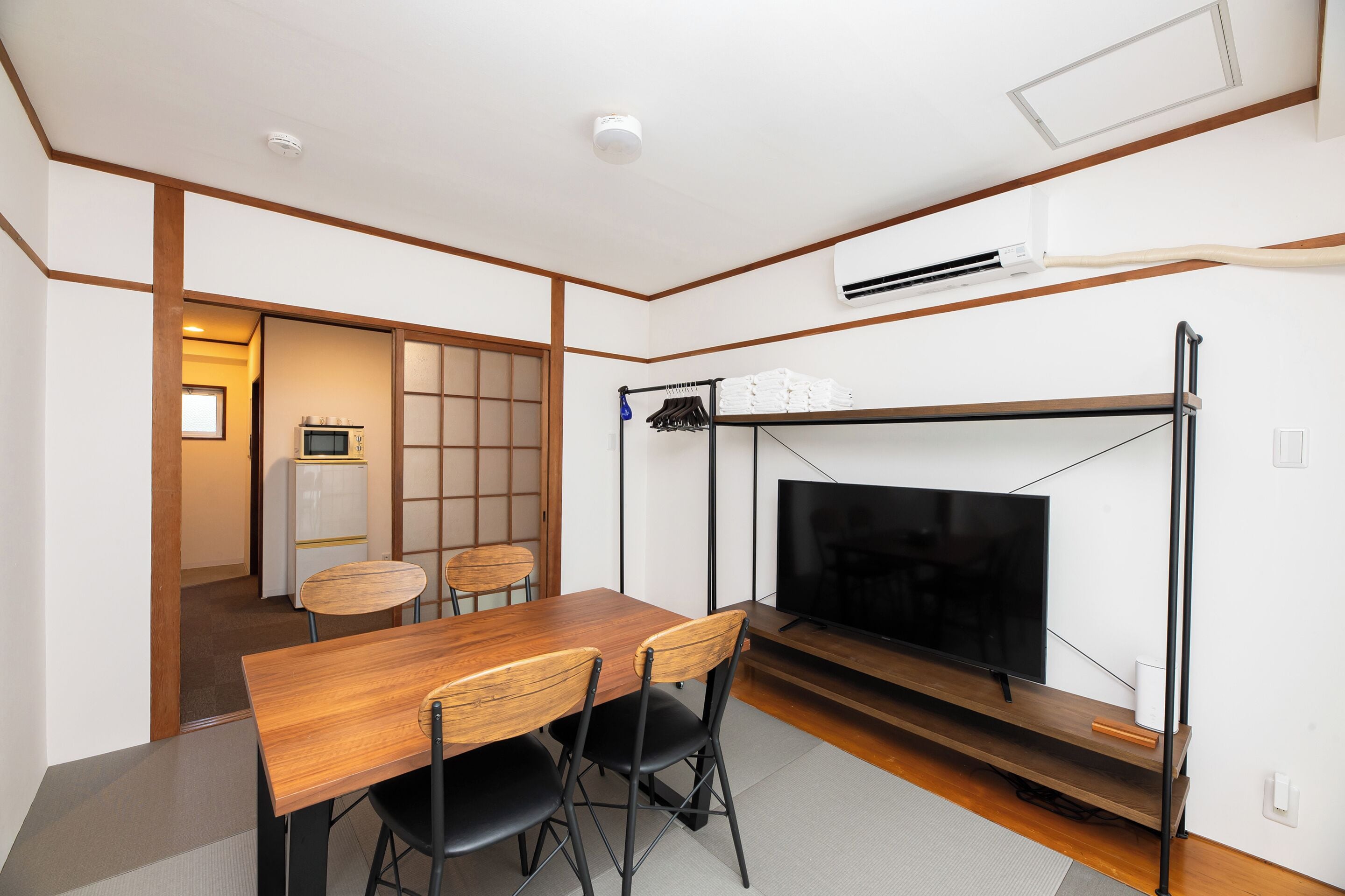 A compact living space with a wooden dining table, black chairs, a television, and a kitchenette.